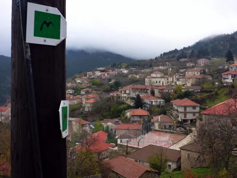 Menalon Trail waymark above the rooftops of Lagkadia under low clouds