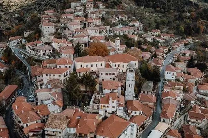 Aerial view of red-roofed stone houses and bell tower of Dimitsana